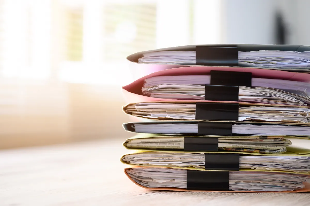 Pila di cartelle e documenti ufficiali in attesa di traduzione su una scrivania d'ufficio
