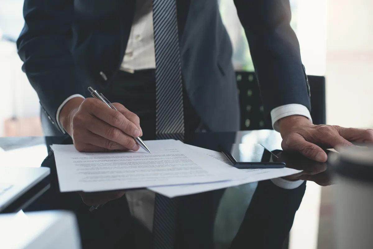 Business professional signing a legal contract at a desk in a corporate office