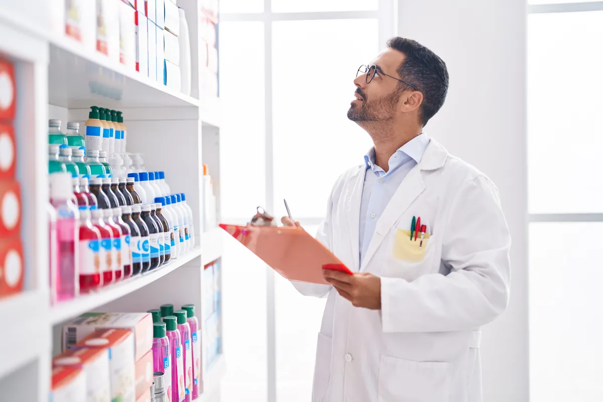 Pharmacist checking medication packaging against pharmacy shelving