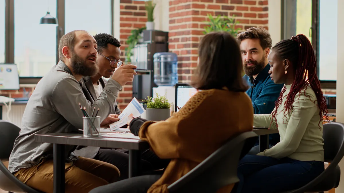 Project team gathered around a table reviewing a printed document and a laptop