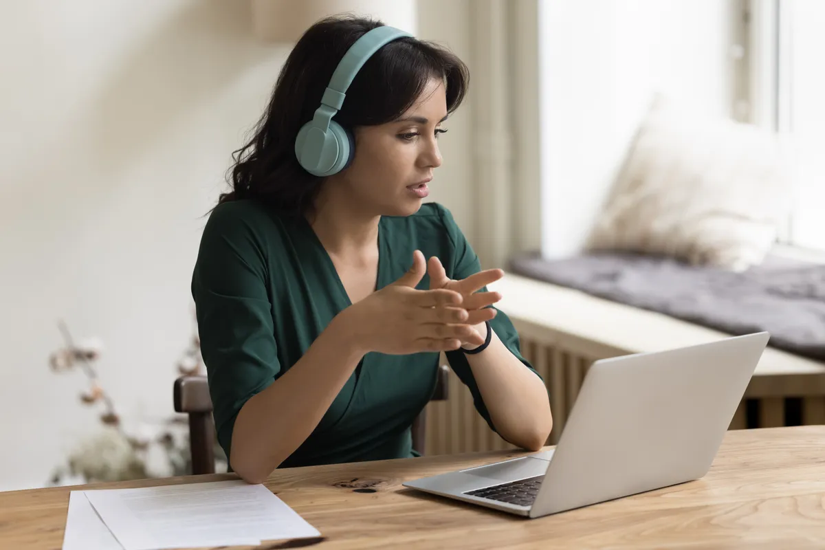 Interpreter wearing headphones and gesturing during a video call on her laptop