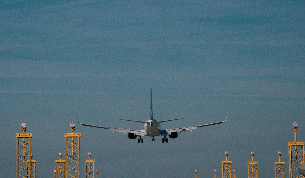 An airliner seen head-on with its landing gear down, descending over a row of yellow approach lighting towers against a dusk sky