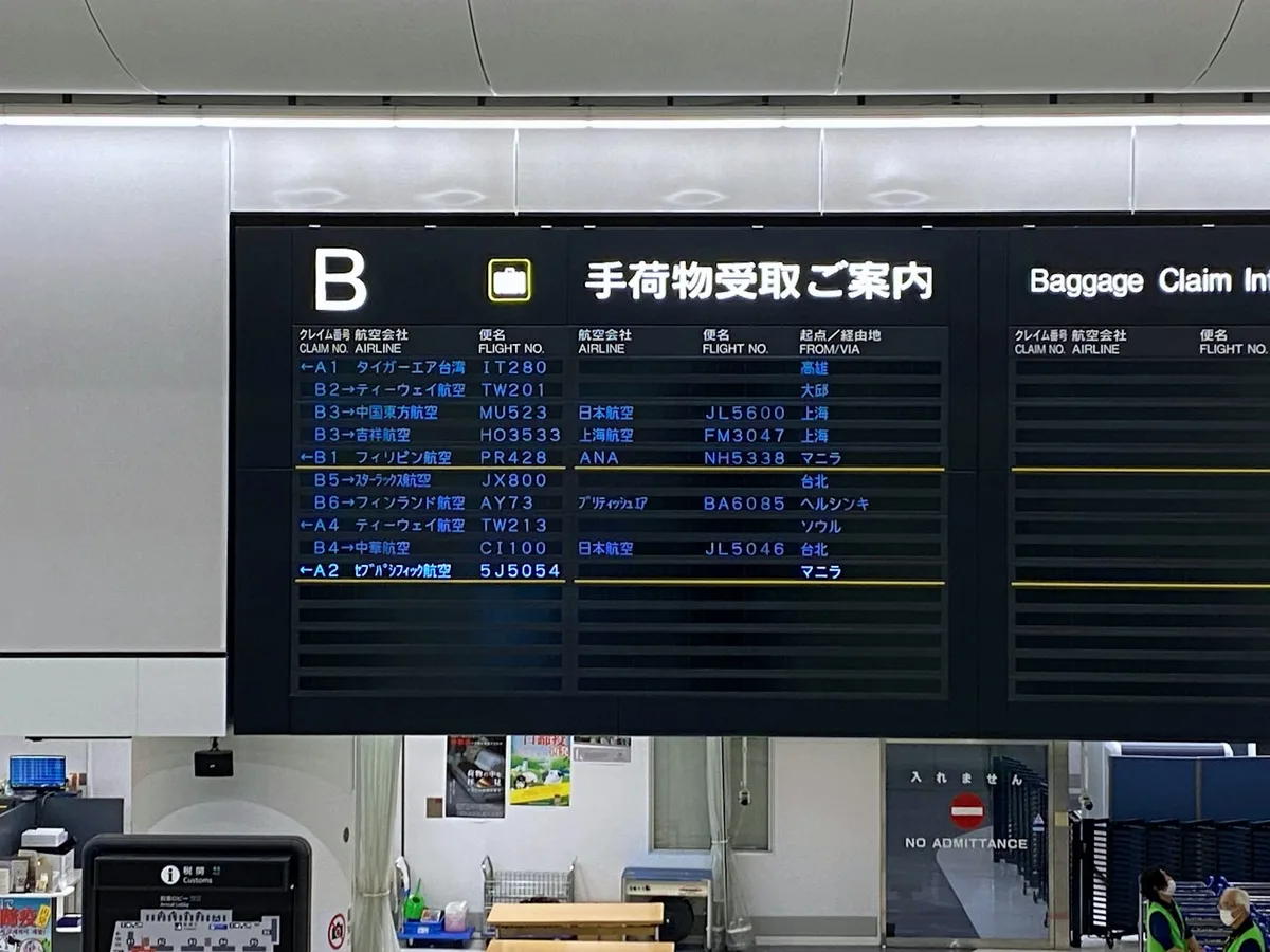 A bilingual airport information board showing the same flight information in Japanese and English