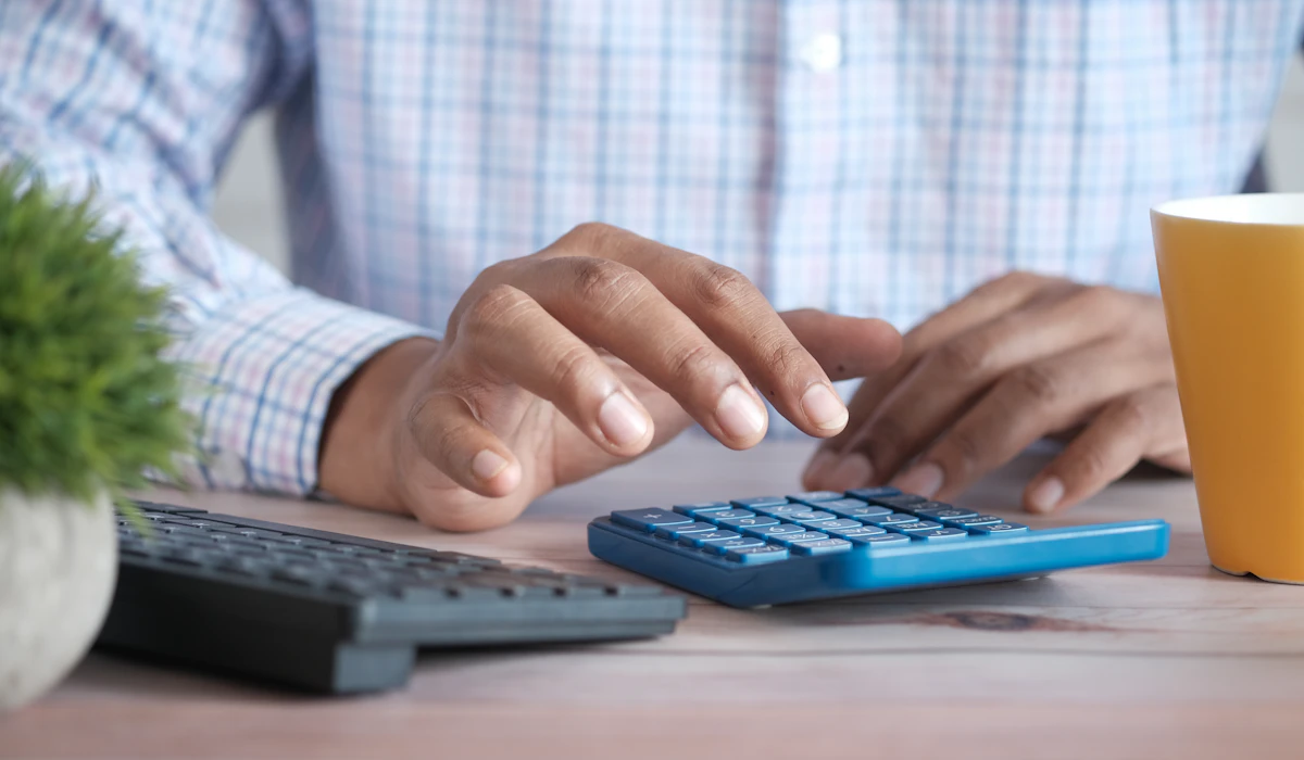 A person working at a desk with a calculator, a keyboard and a mug of coffee