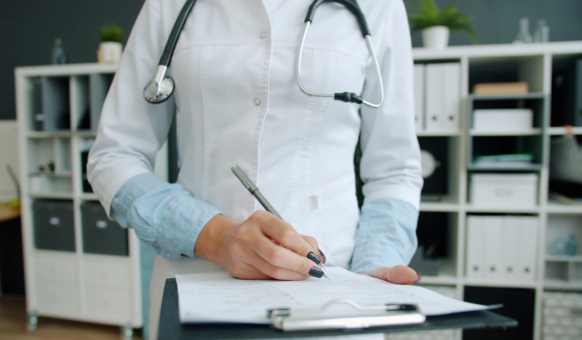 A doctor with a stethoscope writing on a clipboard in an office