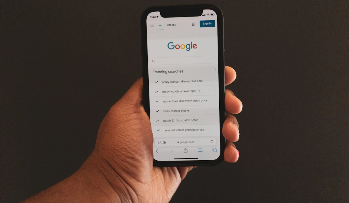 A hand holding a smartphone showing the Google homepage