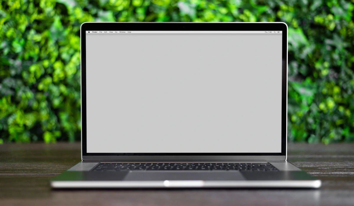Ein aufgeklappter Laptop auf einem Schreibtisch vor einer grünen Pflanzenwand