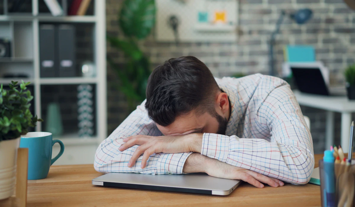 A man sitting at a desk with his head resting on his crossed arms