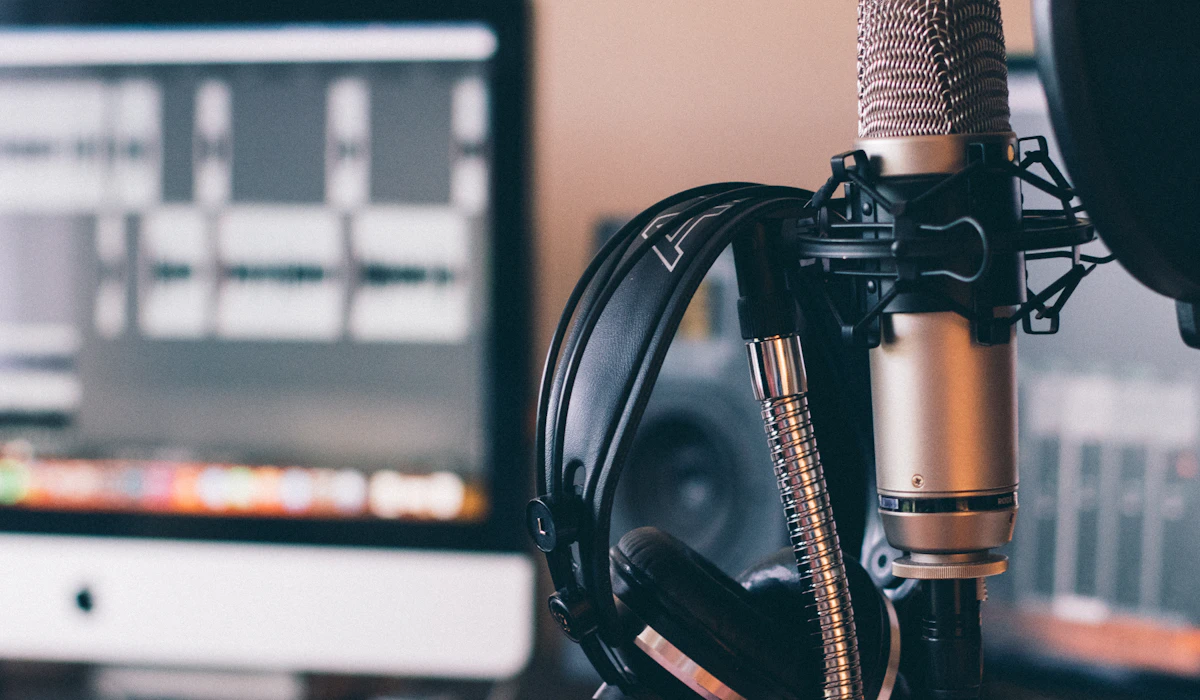A studio microphone and headphones on a desk beside a computer screen