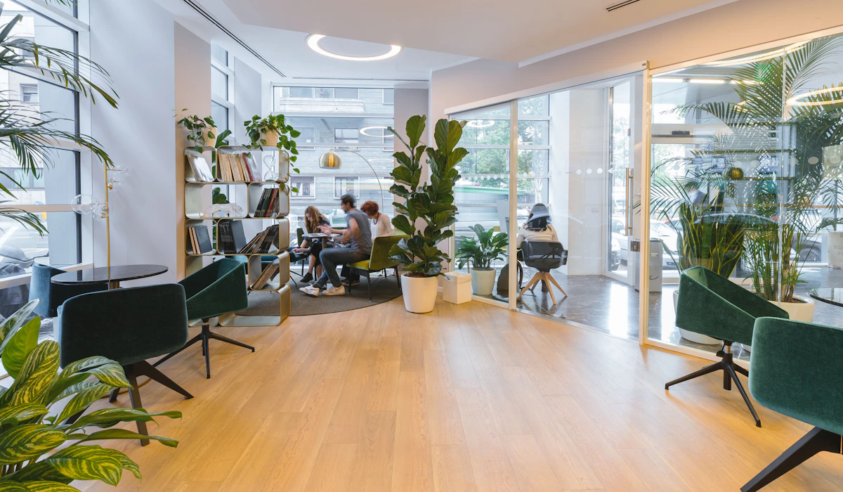 A bright, modern office lounge with green upholstered chairs and potted plants
