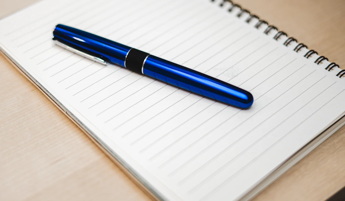 A blue pen resting on an open, lined notebook on a wooden desk