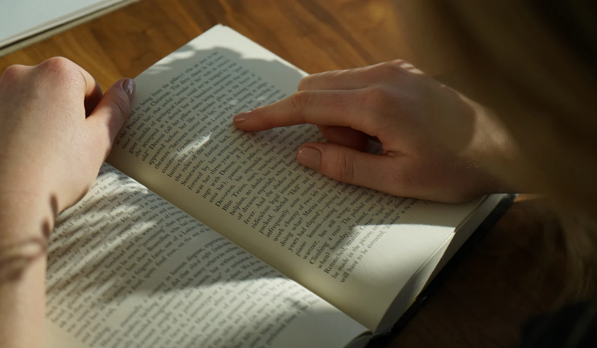 Hands turning the pages of an open book on a wooden table