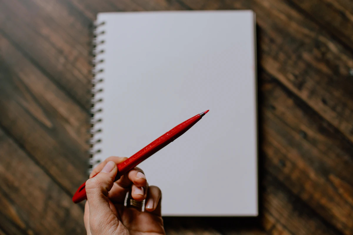 A hand holding a red pen over a blank notepad