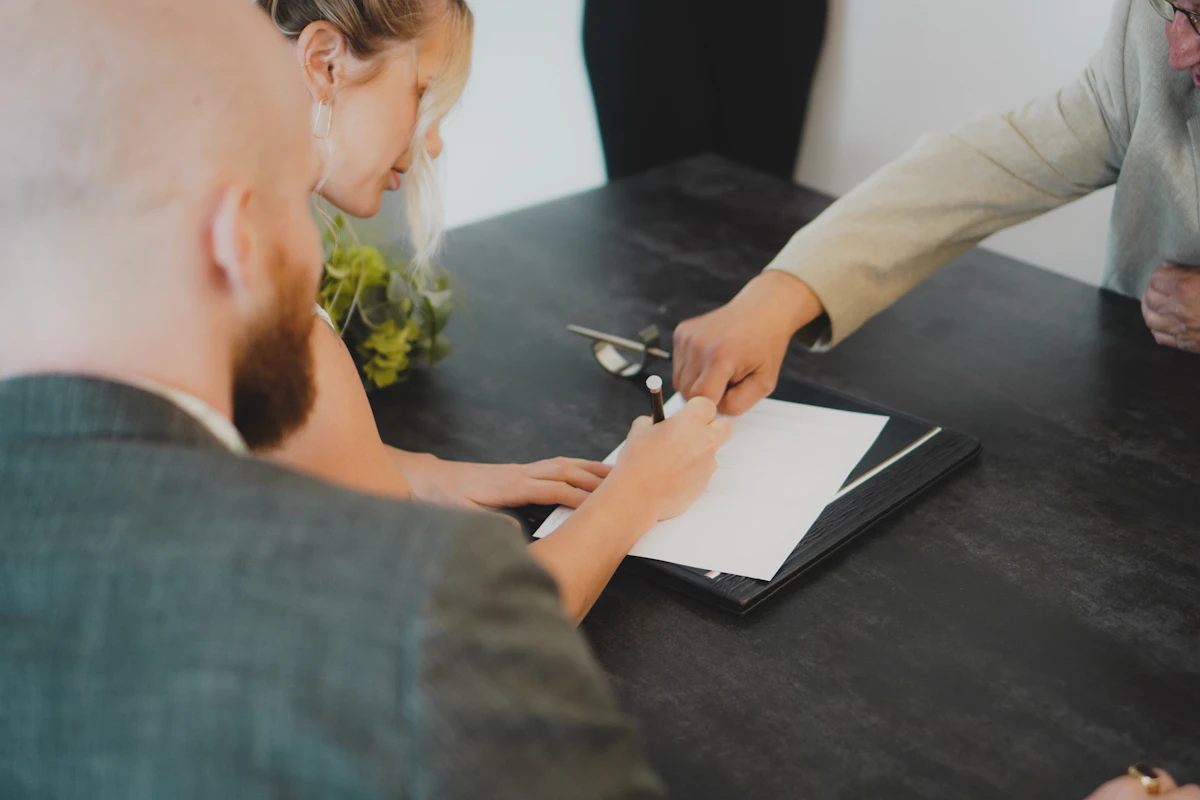 Two people signing a document across a desk while a third looks on