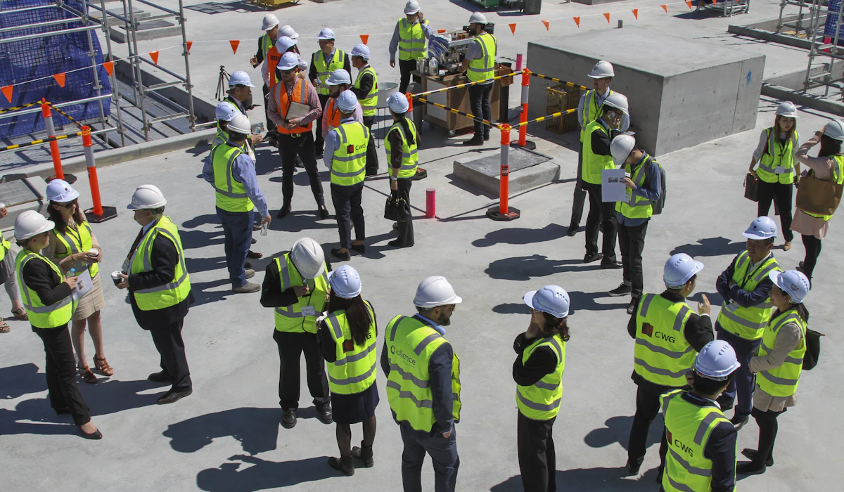 A group of workers in high-visibility vests and hard hats gathered in small clusters for a site safety briefing
