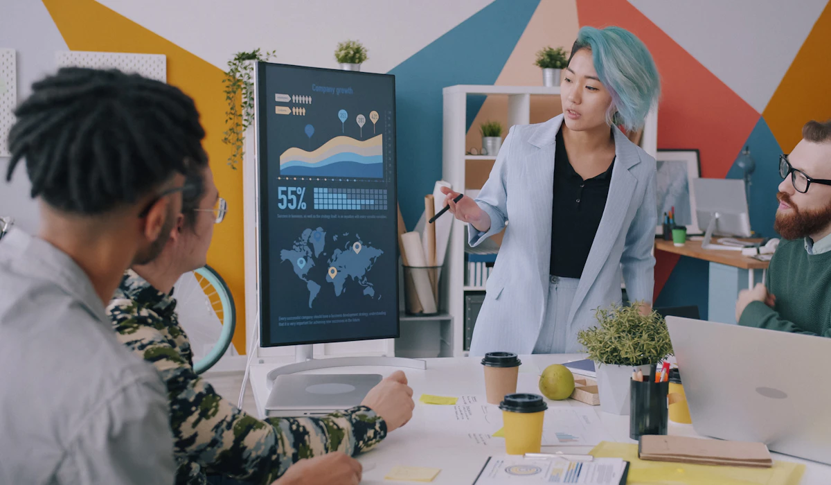 A businesswoman presenting company growth data to colleagues on a digital screen