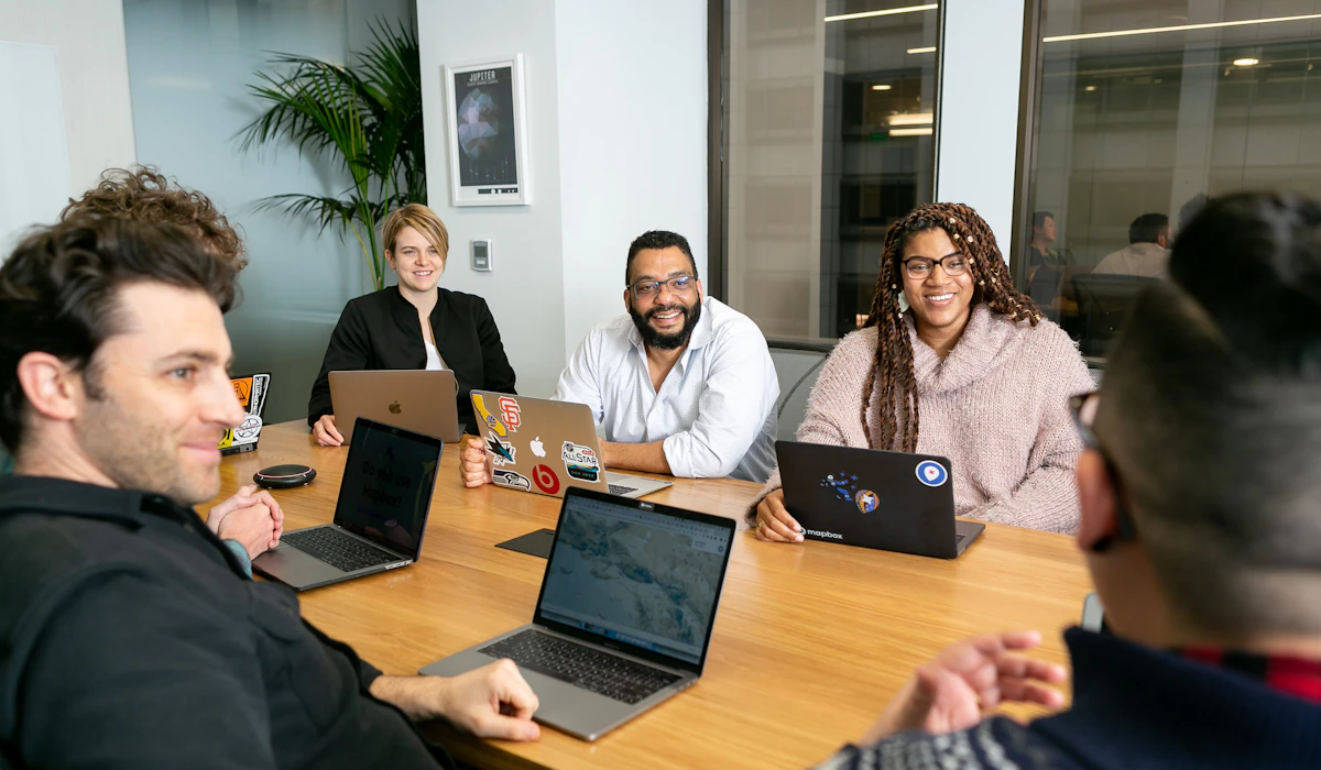 Five colleagues gathered around a boardroom table, each with an open laptop