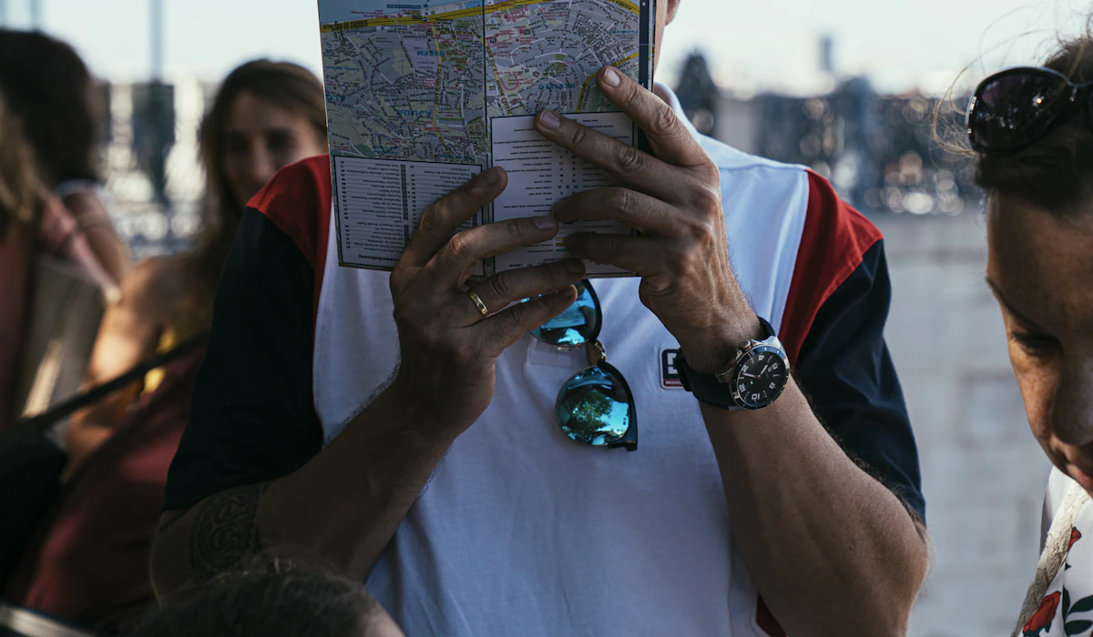 A traveler holding an open paper city map in front of him while standing in a crowd on a sunny street