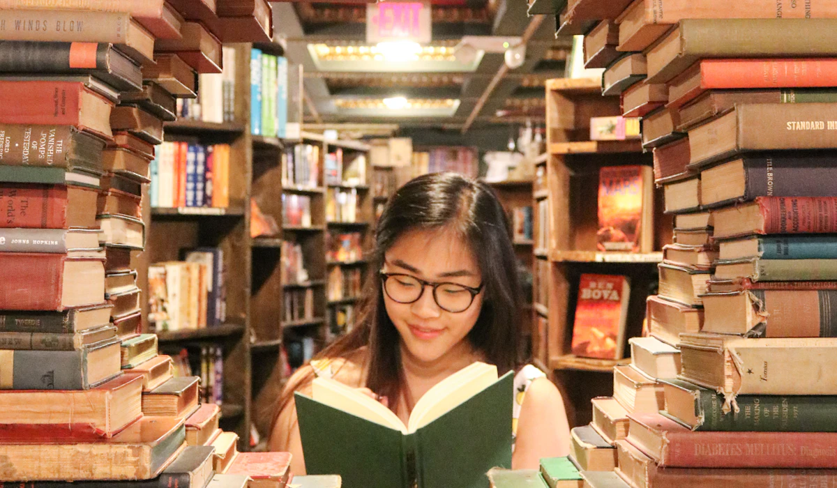 A woman reading a book surrounded by stacks of old books in a bookstore