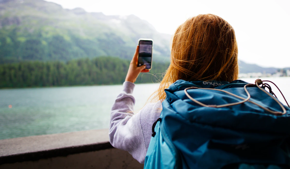 Una donna fotografa un lago di montagna con lo smartphone